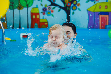 A little boy of 9 months is learning to swim in the pool with a coach.
