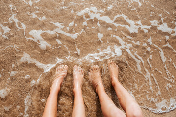 Close up of feet on beach with sea water beneath them. Sea foam and warm water soaking legs.