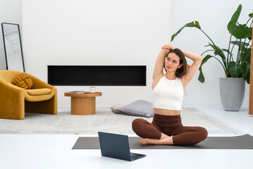 Young woman doing exercise at home and watching online classes using laptop. Sport workout. Concept of healthy lifestyle, female wellness.
