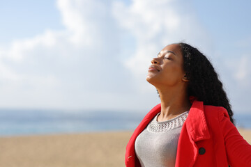Black woman in red jacket breathing on the beach - 785030329