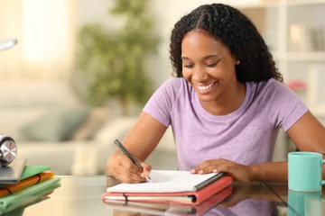 Zelfklevend Fotobehang Happy black student taking notes at home © Antonioguillem
