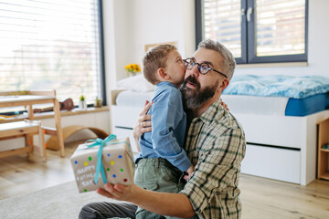 Dad get a handmade gift from little son, present wrapped in diy homemade wrapping paper. Father embracing boy. Happy Fathers day concept.