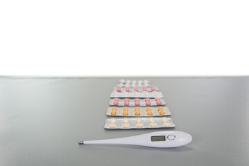 several blisters with pills or vitamins lying in a row with a thermometer on a gray table with copy space background