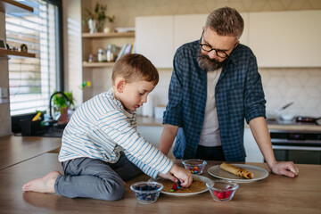 Boy filling pancake with fruit, sweets. Father spending time with son at home, making snack together, cooking. Fathers day concept.