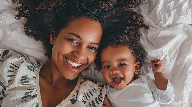 Photo of happy young african american mother with curly hair laying on white bed and playing happily together. Happy Mother's day Image. 