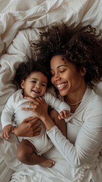 Photo of happy young african american mother with curly hair laying on white bed and playing happily together. Happy Mother's day Image. 