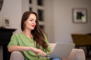 Portrait of a beautiful young woman sitting in an armchair and relaxing at her modern home. Brunette haired woman wearing white shirt and blue jeans.