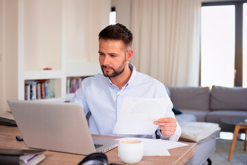 Man with his laptop sitting at desk and working from home - 785042930