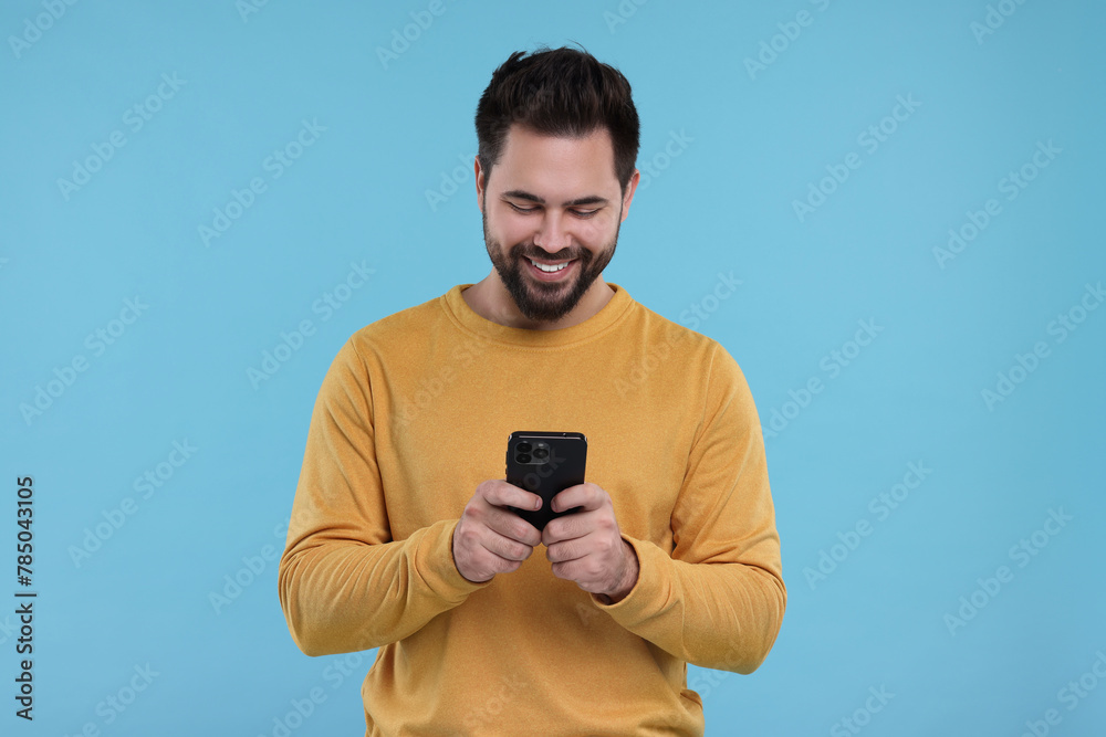 Canvas Prints Happy young man using smartphone on light blue background