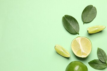 Whole and cut fresh ripe limes with leaves on light green background, flat lay - obrazy, fototapety, plakaty