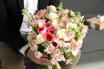Man with beautiful bouquet of flowers on sofa indoors, closeup