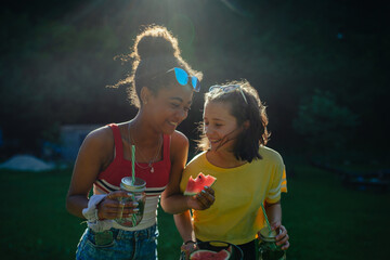 Young teenager girls friends outdoors in garden, eating watermelon.