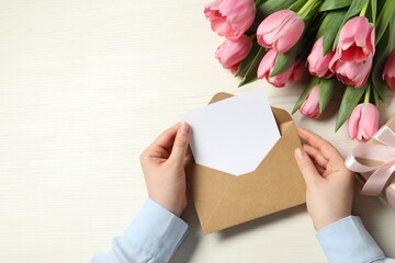 Happy Mother's Day. Woman holding envelope with blank card at white wooden table, top view. Space for text © New Africa