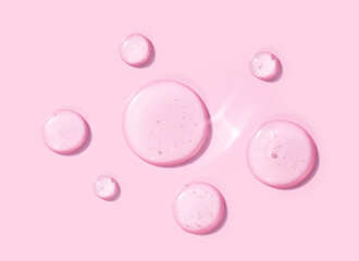 round drops of transparent gel serum on pink background