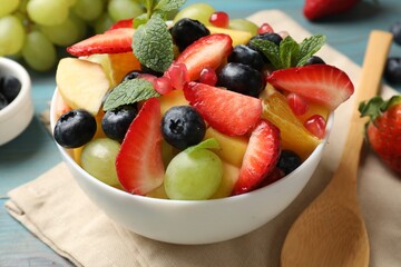 Tasty fruit salad in bowl, ingredients and spoon on light blue wooden table, closeup