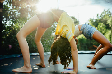 Teenage girls friends outdoors in garden, doing exercise on trampoline, having fun, jumping.