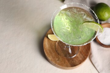 Delicious Margarita cocktail in glass, salt and limes on light table, above view. Space for text