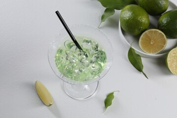 Delicious Margarita cocktail with ice cubes in glass and lime on white table