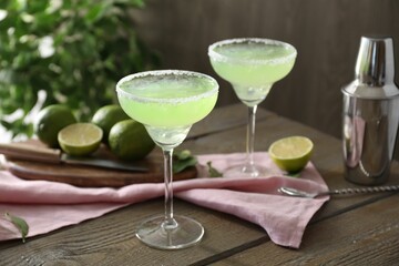Delicious Margarita cocktail in glasses, lime and shaker on wooden table, closeup