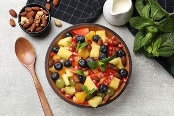 Delicious fruit salad in bowl, nuts and fresh mint on grey table, flat lay