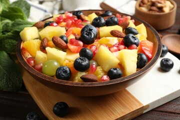 Delicious fruit salad in bowl, berries, nuts and fresh mint on wooden table