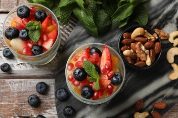 Delicious fruit salad, fresh berries, mint and nuts on wooden table, flat lay