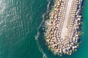 Drone top view of a breakwater with large boulders jutting into the sea. Surrounded by a calm sea....
