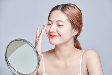 Beauty asian woman face portrait. beautiful model girl with perfect fresh clean skin color lips red. Face care, Cosmetology , beauty and spa. hands touches her face smiling and looking into mirror.