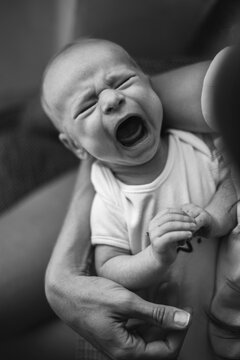 Crying baby boy in mother's arms at home