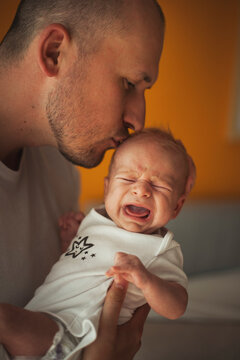 Father kissing crying baby boy at home