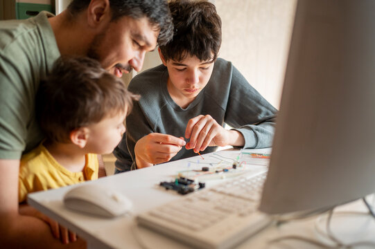 Boy repairing micro controller near father and brother at home