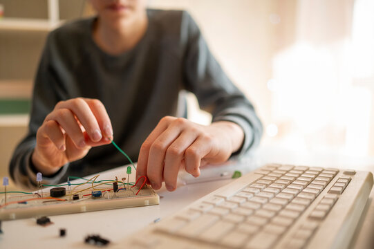 Teenage boy adjusting wires on micro controller at home