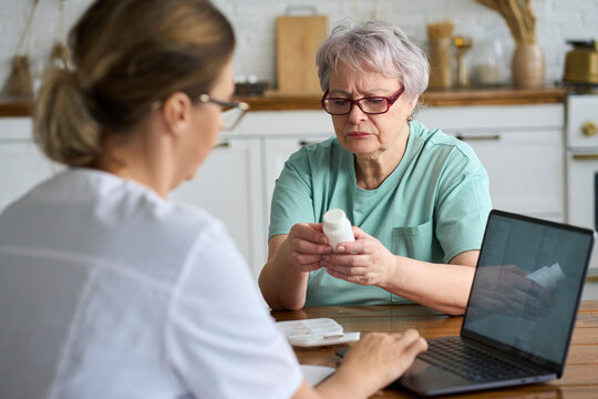 Senior woman holding medicine bottle with nurse using laptop at home