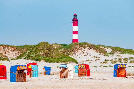 Germany, Schleswig-Holstein, Amrum, Hooded beach chairs on sandy beach with lighthouse in background