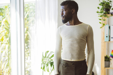 Young non-binary person looking out of window at home