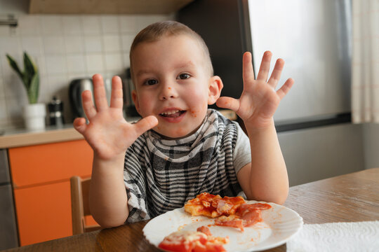Happy boy showing hands near pizza at table in kitchen