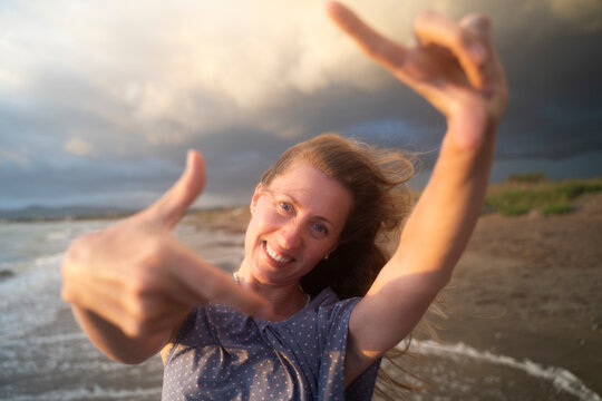 Happy blond woman enjoying sunset making finger frames at beach