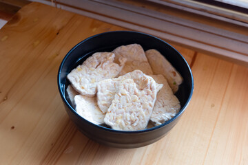raw tempeh in a black bowl being marinated in spices for frying
