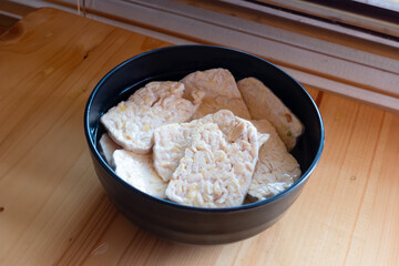 raw tempeh in a black bowl being marinated in spices for frying