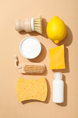 Bowl with soda, lemon, soap, sponge, brush and bottle on beige background, top view