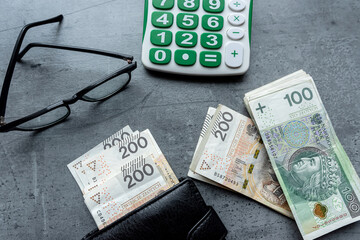 Polish zloty banknotes PLN currency in black wallet wirh calculator glasses in grey desk