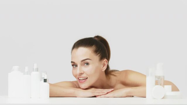 Advertising of spa treatments, anti-aging care products for delicate dry skin. Portrait of an attractive middle-aged woman next to mock-ups of jars of cream and cosmetology natural cosmetics.