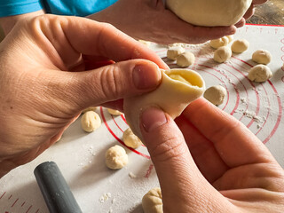 Unrecognizable female hands sculpts dumplings food from dough and potatoes in the kitchen