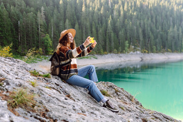 Woman using her phone for video call on the mountain. Selfie time. Enjoying nature alone and taking picture on smartphone.  Lifestyle, adventure, nature.