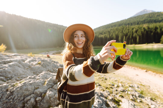 Woman using her phone for video call on the mountain. Selfie time. Enjoying nature alone and taking picture on smartphone.  Lifestyle, adventure, nature.