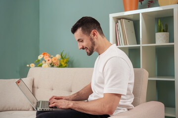 Young man working with laptop on sofa at home indoors.