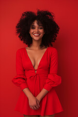 Fototapeta premium woman in studio, full body, wearing red dress trand up front of camera smiling having curly black hair beautiful smile photo showing full body on solid isolated red backround, studio light
