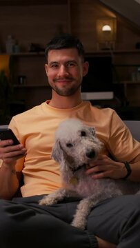 Man sitting on couch with Canidae, holding Carnivore breed dog, using cell phone