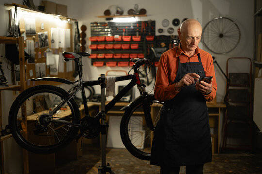 Elderly man using a smartphone in a bicycle repair shop