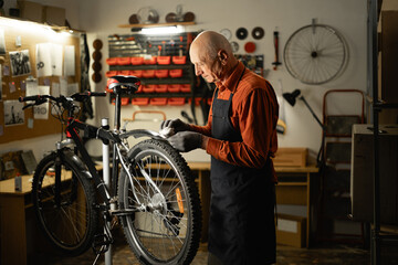 Old man cleaning mountain bike in garage or repair workshop. Bicycle Maintenance